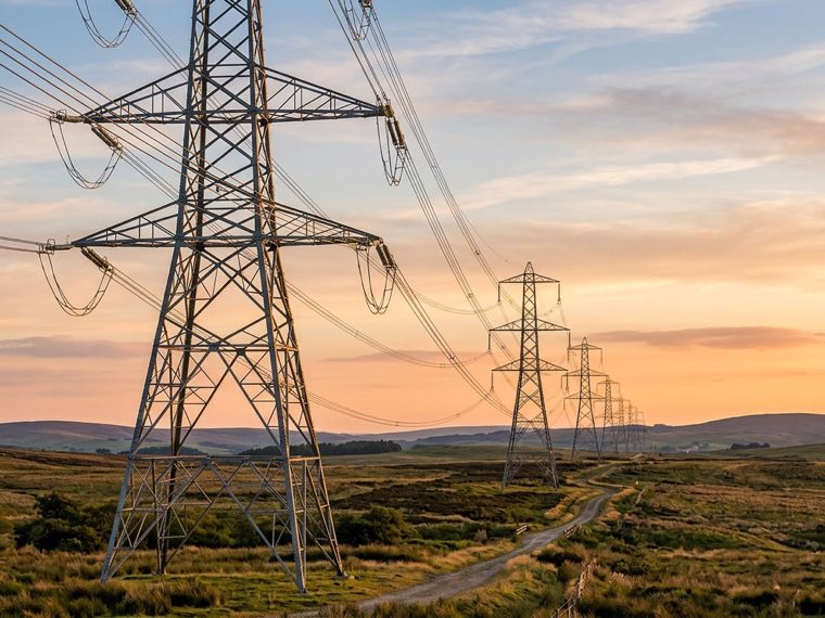 High-voltage transmission towers crossing open country at dusk