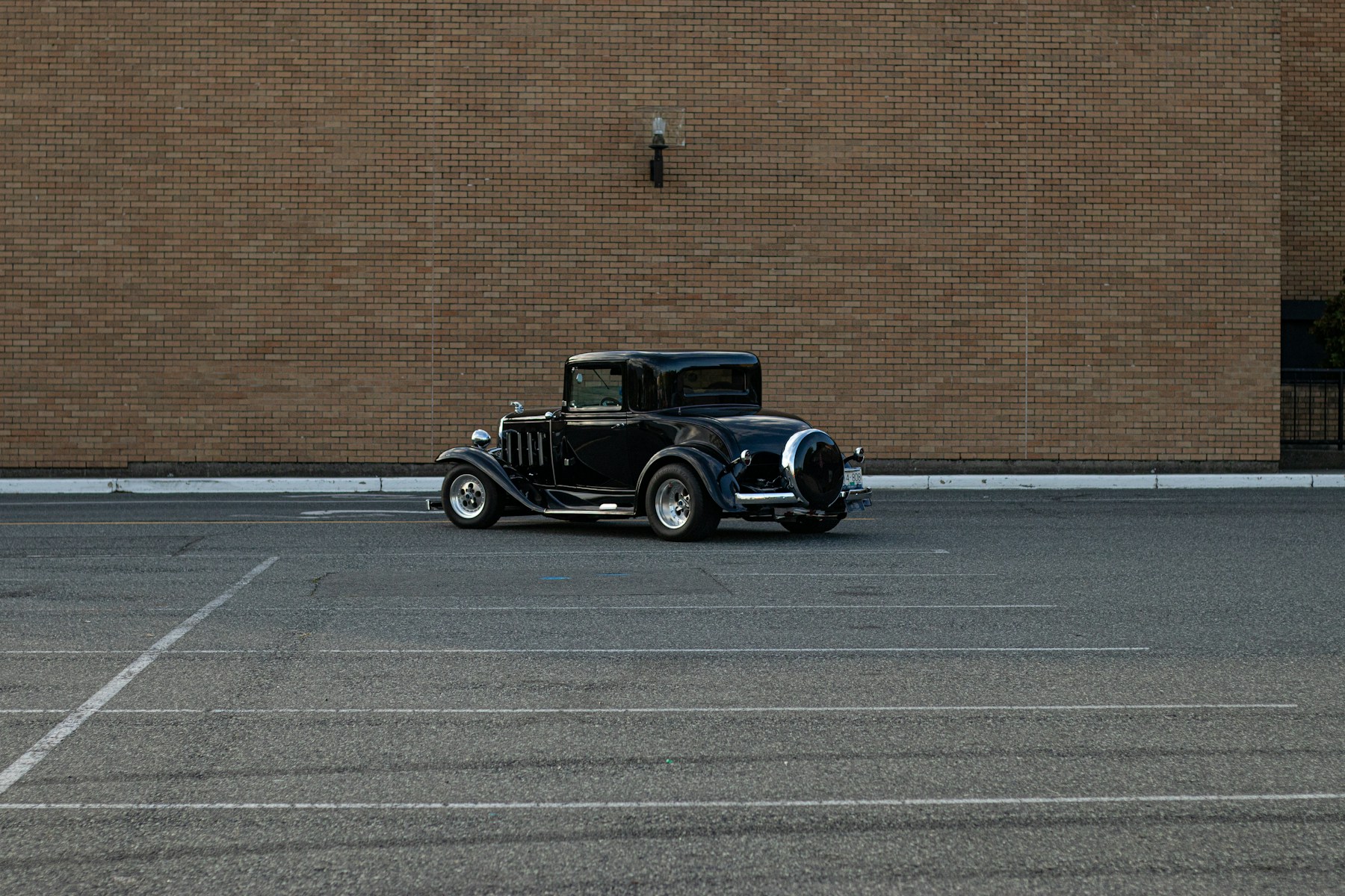 A restored early automobile parked beside a brick building